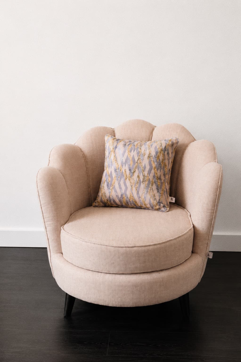Cream scalloped shell-back NDB accent chair with a patterned cushion on a dark floor.