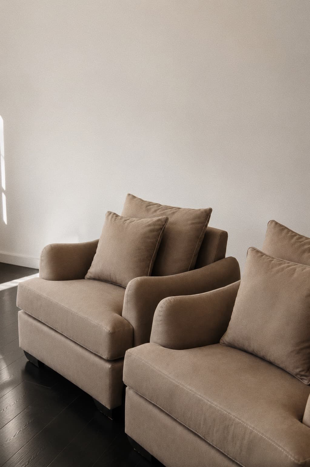 A matched pair of taupe NDB armchairs against a pale wall on a dark timber floor.